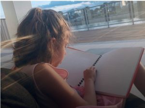 Eva reading a Braille Book in the sunshine on a balcony