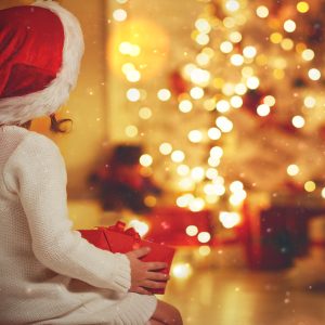 A child looking at a Christmas tree with a santa hat on.